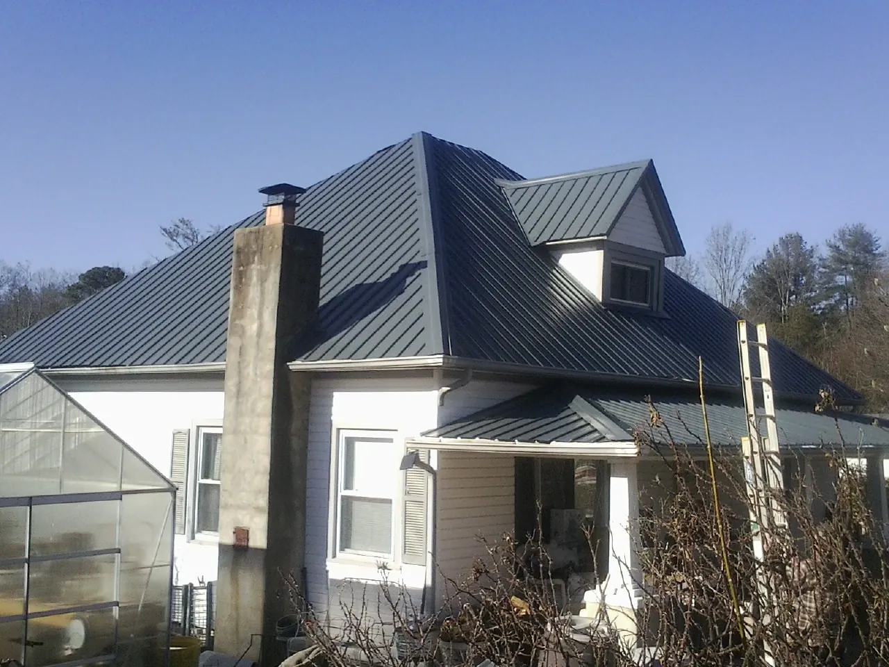 Dark blue standing seam metal roof on a white farmhouse with dormer — Slate & Tile Roof Repair by Roofing Brothers in Keyes