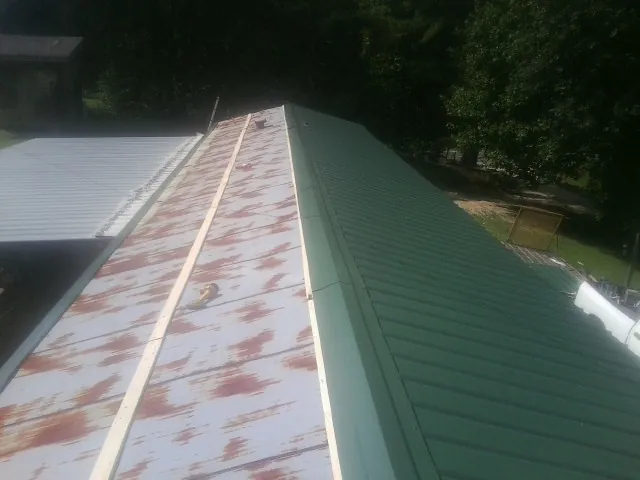 Old rusted panels beside newly installed green metal roofing — Wind Damage Roof Repair by Roofing Brothers in Keyes